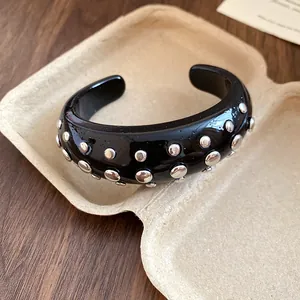 Close-up of black resin cuff bracelet featuring silver round metal studs