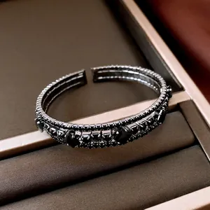 Vista detallada de un brazalete abierto multicapa con diamantes negros en bandeja terciopelo