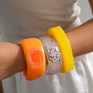 Close-up of three chunky resin bangles in vibrant orange, glitter, and yellow colors.