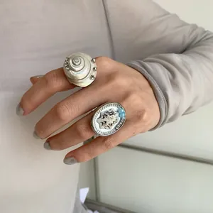Detailed view of large geometric shell rings with rhinestones on an index finger.
