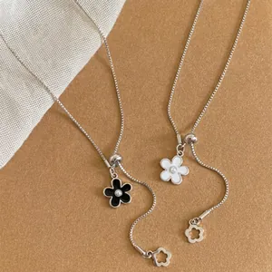 Detailed view of minimalist flower pull necklaces with black and white enamel charms