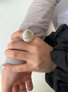 Detailed close-up view of a minimalist geometric seashell ring worn on an index finger.