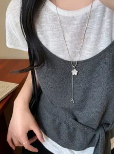 Detail of a minimalist silver-toned flower adjustable necklace worn over a grey knit sweater