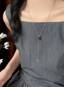 Detail of silver-toned Y-necklace with black flower and star pendants on a model.