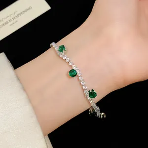 Close-up view of a silver tennis bracelet with emerald green zircons on a female wrist