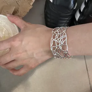 Dettaglio di un bracciale rigido aperto argento con design traforato al polso.