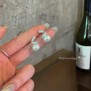 Detailed close-up of elegant pearl stud earrings with sparkling pavé zircon accents.