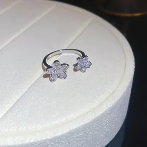 Close-up detail of a silver open ring featuring two sparkling zircon flower charms on a tray