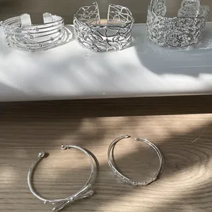 Selezione di bracciali aperti in argento con motivi traforati e fiocchi su fondo in legno.