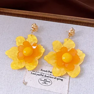 Detalle de pendientes de flores de resina amarilla y naranja vibrantes con agujas de plata.
