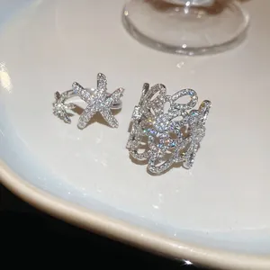 Primo piano di anelli a forma di fiore e stella marina con zirconi su piatto bianco