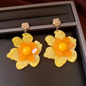 Primer plano de pendientes florales de resina amarilla con textura jaspeada y rosas de oro