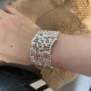 Dettaglio di un elegante bracciale a polsino in pizzo argento traforato indossato al polso