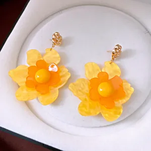 Primer plano de elegantes pendientes de flores de resina amarilla con pernos dorados