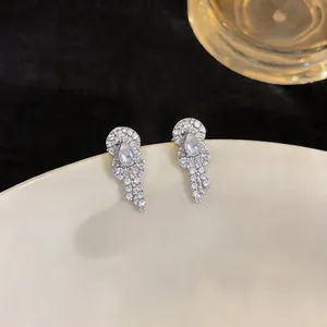Close-up of elegant silver zircon earrings with pear-shaped stone on a white plate.
