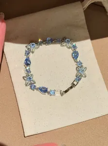 Macro detail of a silver-toned bracelet with blue waterdrop zircon and flower charms