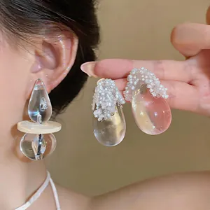 Vista dettagliata di orecchini a goccia in resina trasparente con delicate perline bianche.