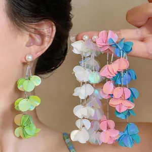 Dettaglio macro di eleganti orecchini a nappa con petali colorati cangianti e perle bianche