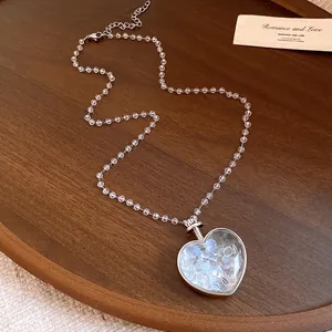 Primo piano squisito di una collana di perle con ciondolo a cuore e pietre azzurre.