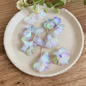 Orecchini a nappa con petali iridescenti e aghi d'argento presentati su un piatto di ceramica