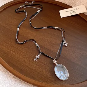 Dettaglio di una collana con ciondolo ovale in pietra blu e charm a forma di croce.