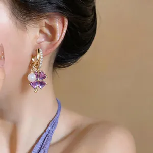 Close-up detail of a French style gold hoop earring with purple clover and pearl charms