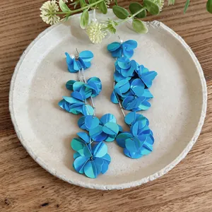 Orecchini a nappa con petali blu a strati su un piatto decorativo in ceramica ruvida