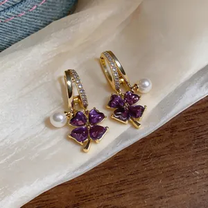 Close-up detail of elegant purple flower earrings with white pearls and gold hoops