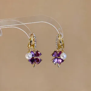 Macro detail of gold four-leaf clover earrings with purple crystal hearts and pearls
