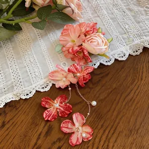 Vista dettagliata di un elegante fermaglio con fiori di stoffa rosa, nappe di perle e catene.