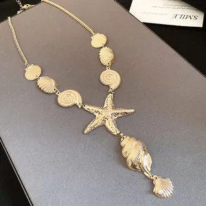 Close-up of gold starfish and seashell charm necklace on a grey jewelry display board.