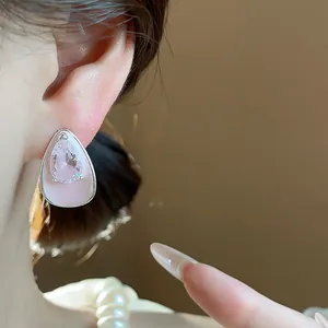 Close-up view of a pink enamel teardrop earring with a sparkling zircon inlay on an ear.