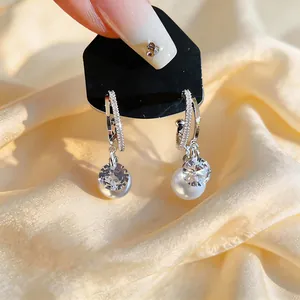 Close-up of elegant silver needle C-shape earrings with zircon and pearl charms