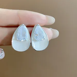 Close-up of elegant teardrop stud earrings with clear zircon and white enamel finish