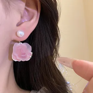 Nahaufnahme eines rosa Rosenohrrings mit Perlenstecker am Ohr eines Modells