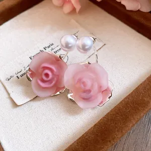 Detailaufnahme von süßen rosa Rosen- und Perlenohrsteckern auf Vintage-Hintergrund.