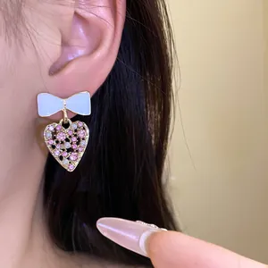 Detaillierte Nahaufnahme von weißen Schleifen- und rosa Herz-Ohrringen am Modelohr