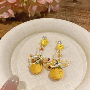 Elegant yellow floral tassel stud earrings with tulip-shaped pendant on wooden plate