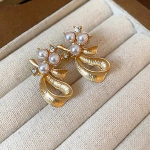 Elegant gold bow stud earrings featuring white pearls and crystals on a velvet tray