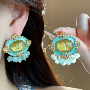 Close-up detail of vintage style oval resin stud earrings with turquoise borders and bead tassels