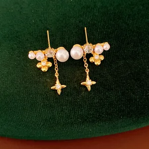 Dettaglio di orecchini dorati con fiori, stelle, perle e zirconi incastonati a mano.