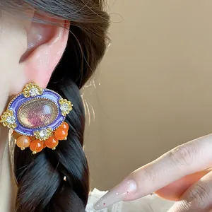 Close-up of vintage style oval purple enamel stud earring with orange beads on model ear