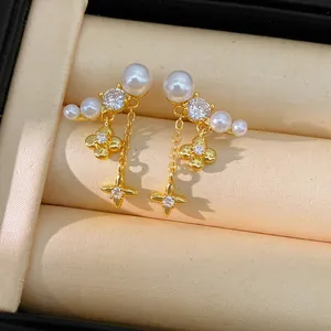 Dettaglio di orecchini placcati in oro con perle, zirconi e nappe a forma di stella