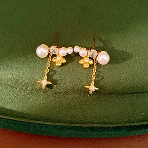 Dettaglio di orecchini placcati in oro con perle, fiori di zircone e stelle cadenti
