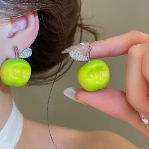 Vibrant green apple stud earrings featuring crystal leaves shown on model ear and hand