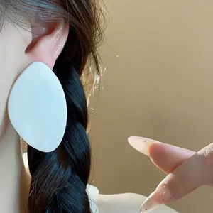 Gros plan d'une grande boucle d'oreille géométrique en résine blanche sur l'oreille