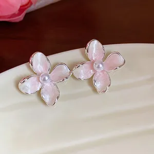 Dettaglio degli orecchini a fiore in smalto rosa con perle centrali su un vassoio di ceramica.