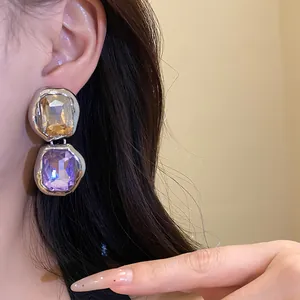 Close-up of silver-tone earrings with amber and purple square gemstones on a model