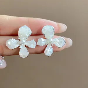 Primo piano di orecchini a fiore in smalto bianco con perle tenuti sulla punta delle dita