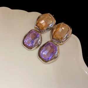 Macro view of elegant square pendant earrings featuring amber and purple faceted gemstones.